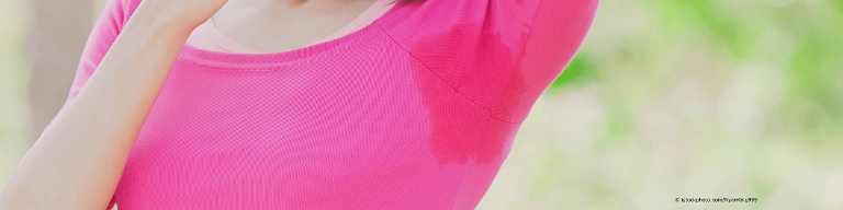 Frau mit Hyperhidrose zeigt ihren Achselschweiß auf pinkem Pulli. Die Stärke des Schwitzens lässt sich mit der Gravimetrie bestimmen.