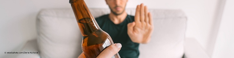 Junger Mann macht einen Alkoholentzug und lehnt eine Flasche Bier mit einer Stopp-Handbewegung ab.