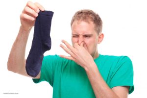 Unter Bromhidrose leidender Mann betrachtet mit zugehaltener Nase seine übel riechende Socke.