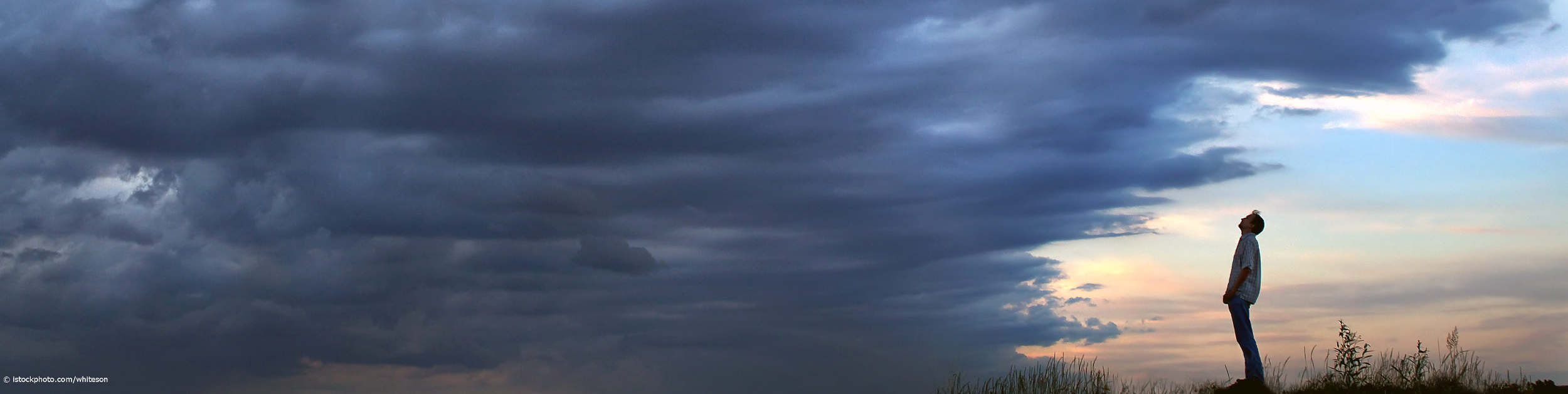 Resilienter Mann steht im Licht und schaut auf eine dunkle Wolkenwand.