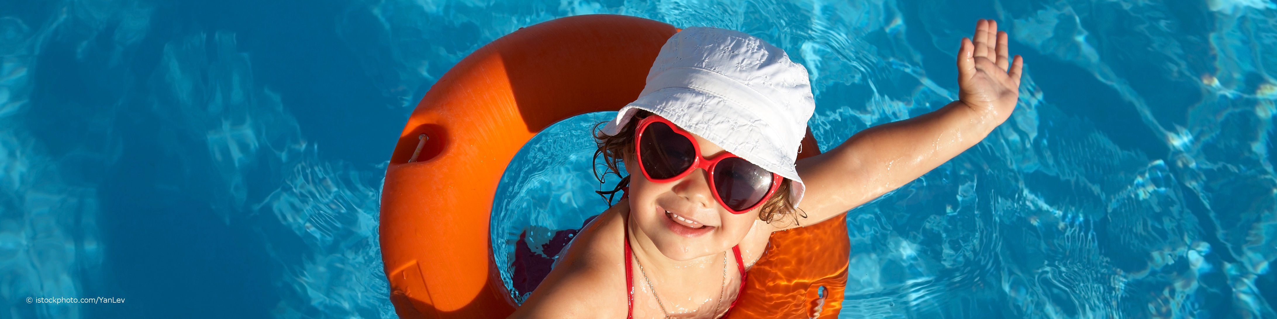 Kind trägt eine Sonnenbrille mit UV-Schutz, einen Hut und einen Schwimmreifen und winkt aus dem Wasser im Schwimmbad