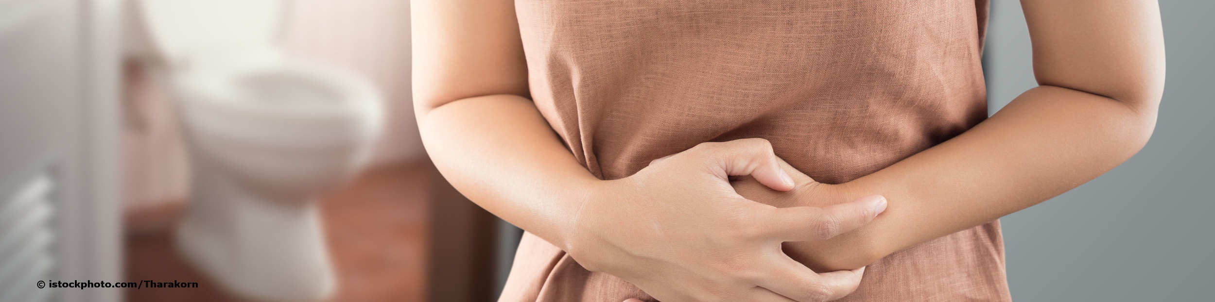 Frau mit Schmerzen beim Wasserlassen hält sich den Bauch und meidet den Toilettengang.