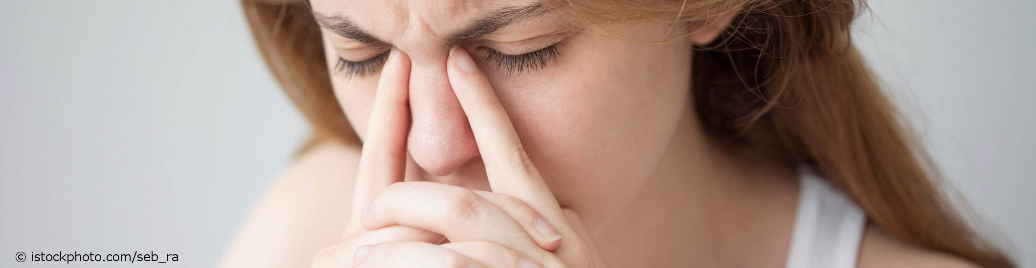 Junge Frau mit Cluster-Kopfschmerz drückt mit ihren Zeigefingern zwischen Nase und inneren Lidrändern