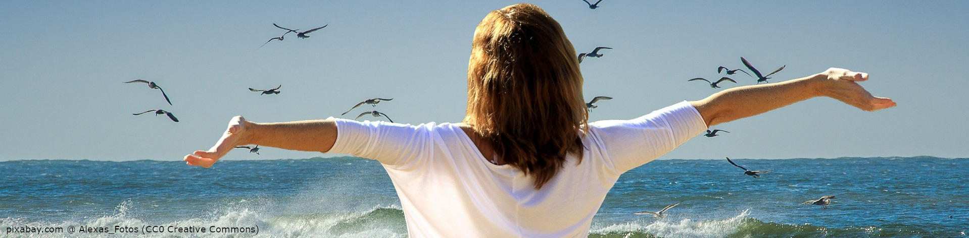 Frau steht mit ausgebreiteten Armen am Strand